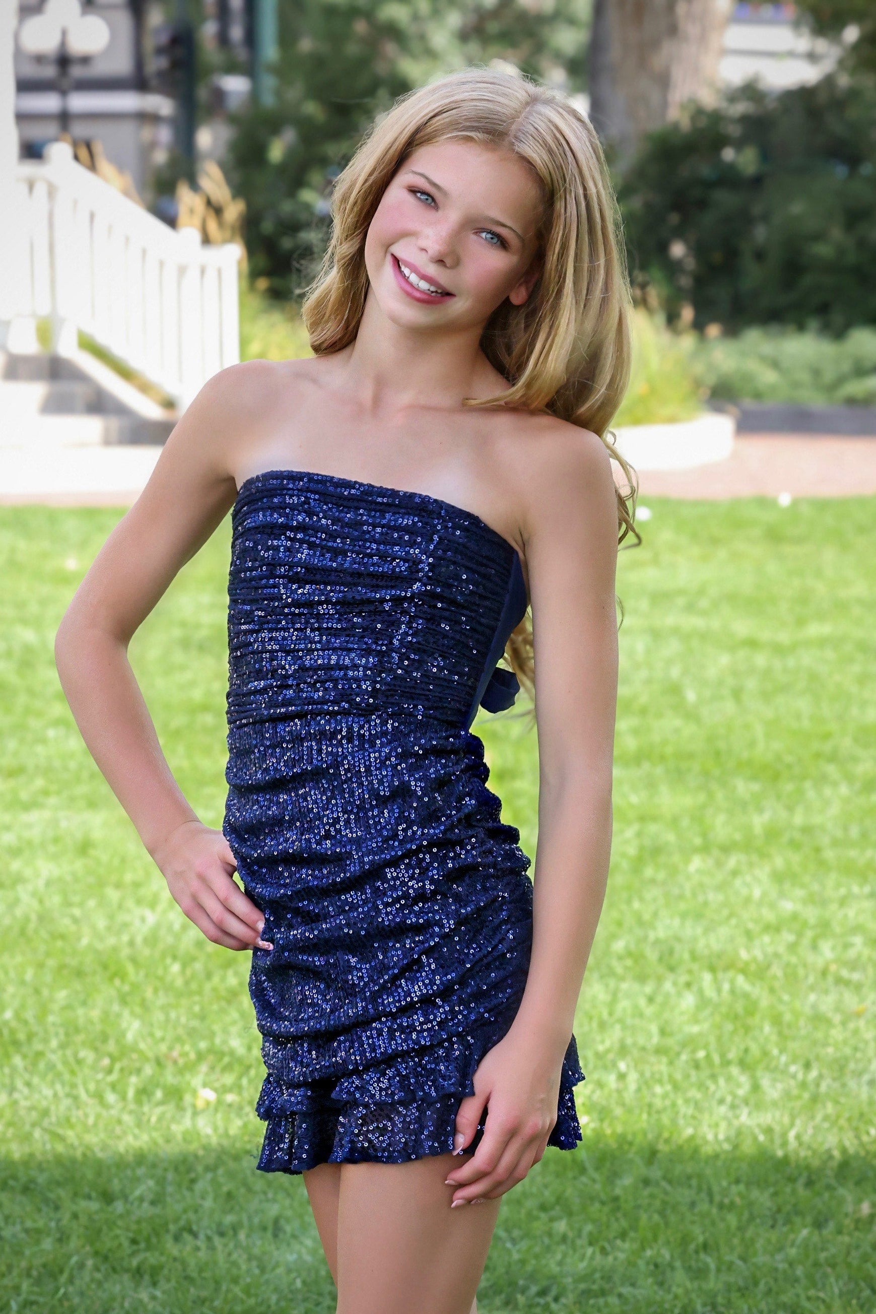 Young woman in a blue strapless dress standing outdoors on grass
