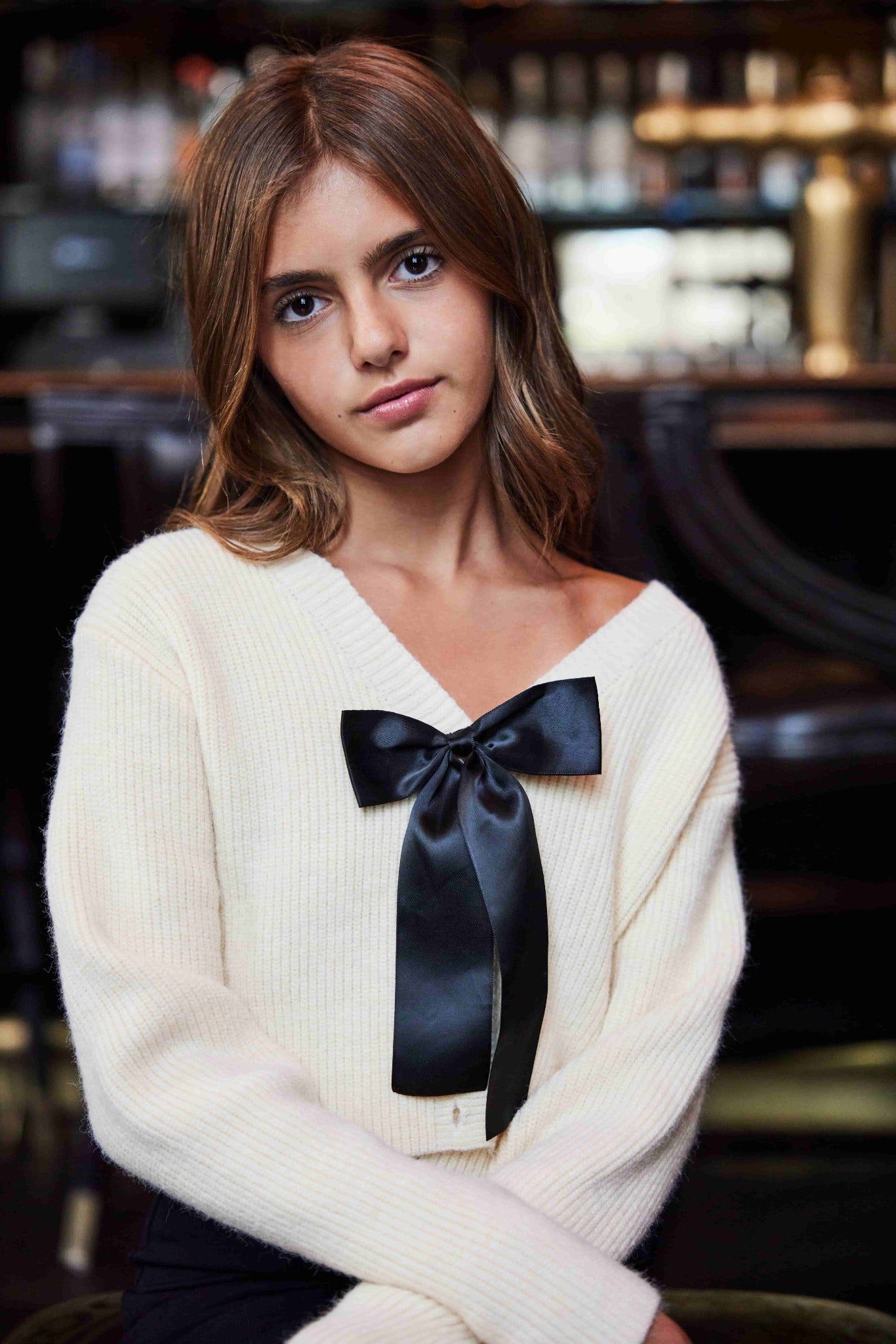Woman wearing a white sweater with a black ribbon in a bar setting
