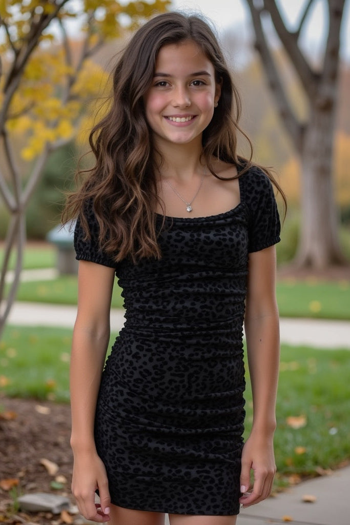 Young woman in a black dress standing outdoors with trees and grass in the background