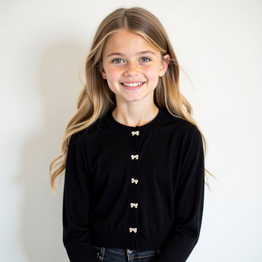 Young girl wearing a black cardigan with white buttons against a plain background